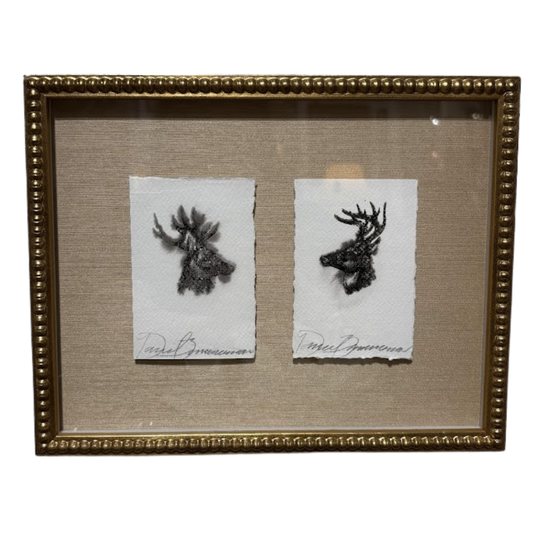 Two black and white prints of deer heads in a gold frame on a beige background