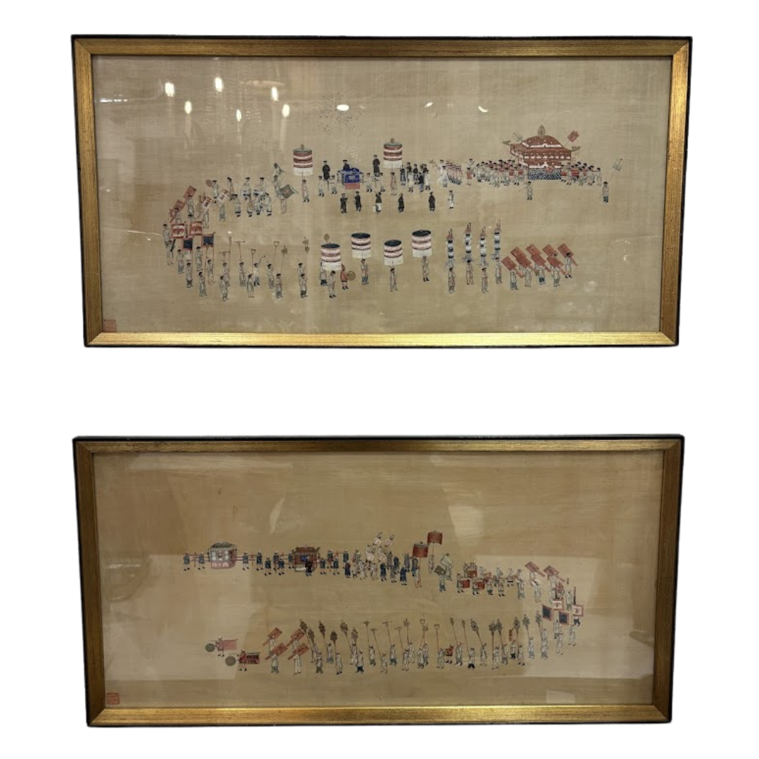 Two framed embroidered artworks depicting a scene with figures and buildings on a beige background.
