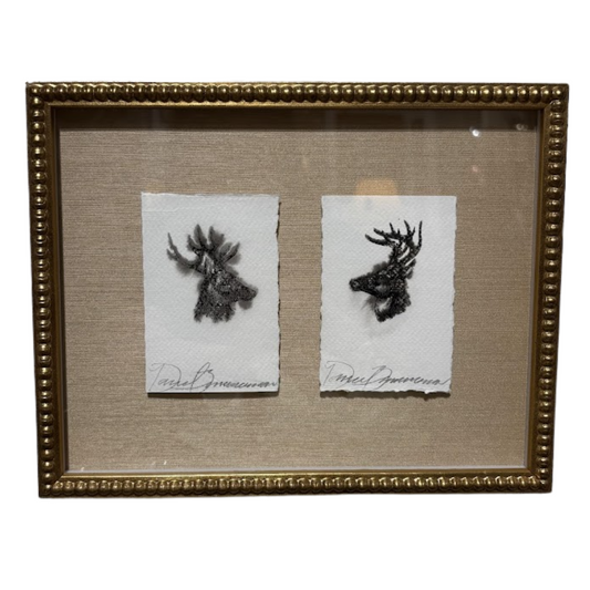 Two black and white prints of deer heads in a gold frame on a beige background