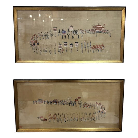 Two framed embroidered artworks depicting a scene with figures and buildings on a beige background.