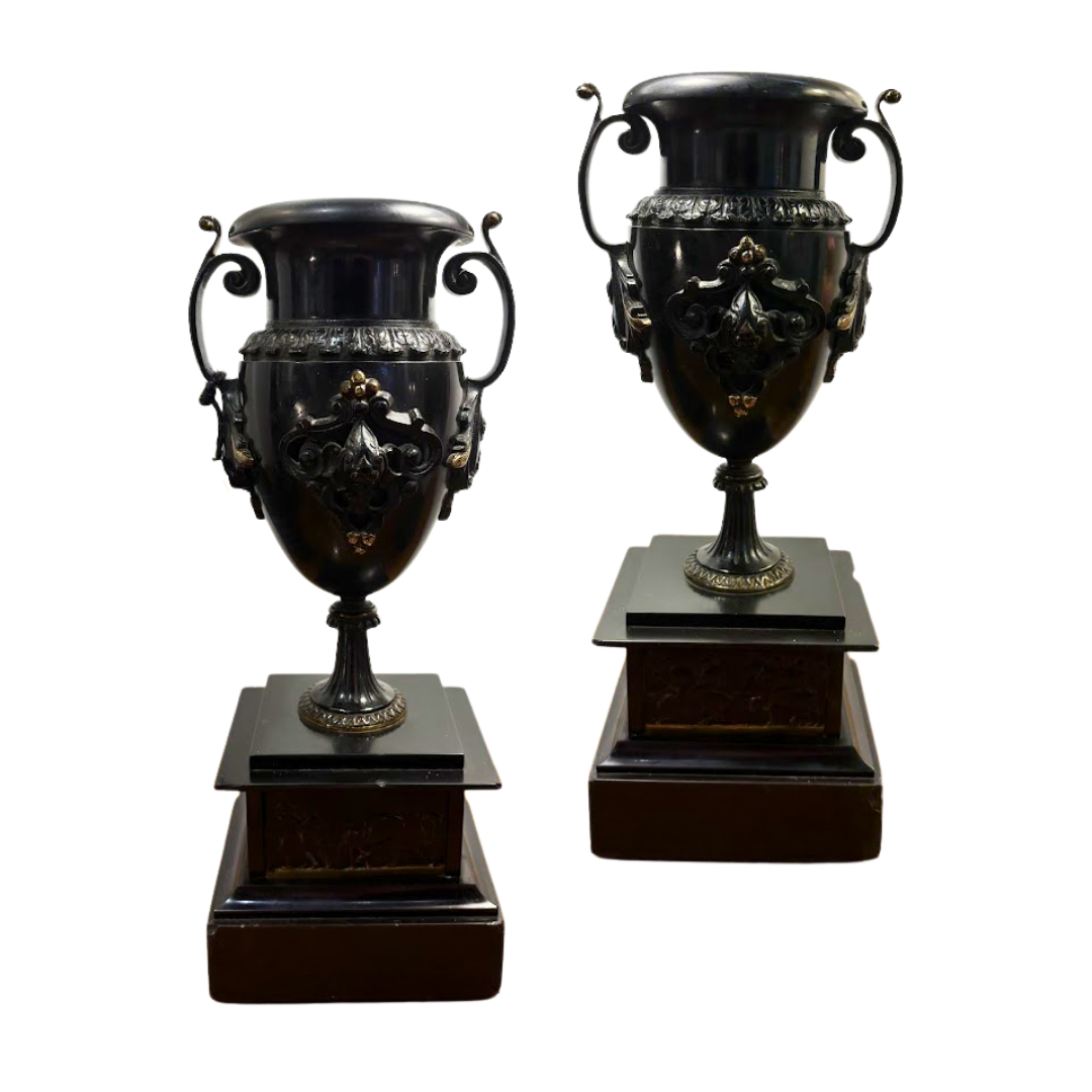 Two ornate black urns on wooden bases against a white background