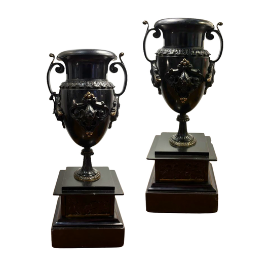 Two ornate black urns on wooden bases against a white background